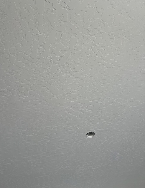 Close-up of a textured ceiling with broad overlapping patterns and a small round fixture opening.