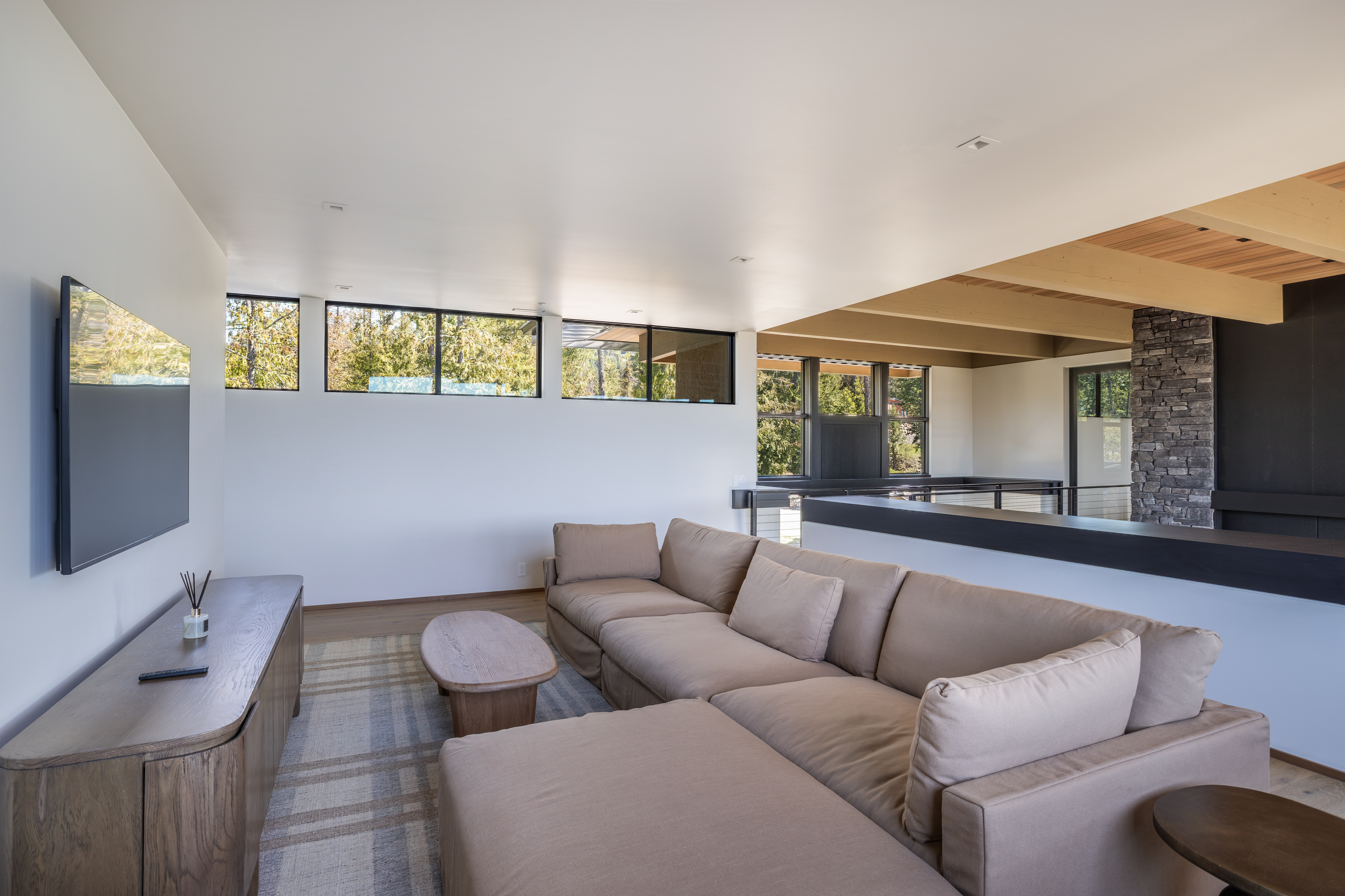 Living room with a tan sectional, wall-mounted television, white walls, and high horizontal windows.