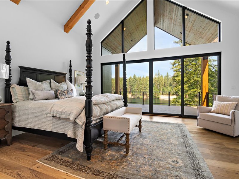 Bedroom with a four-poster bed, vaulted ceiling beams, and sliding doors opening to a deck.